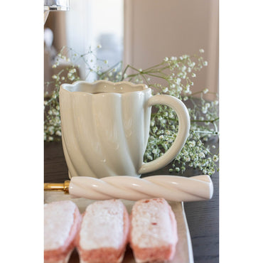 White ceramic mug with decorative handle on a table with flowers and pastries