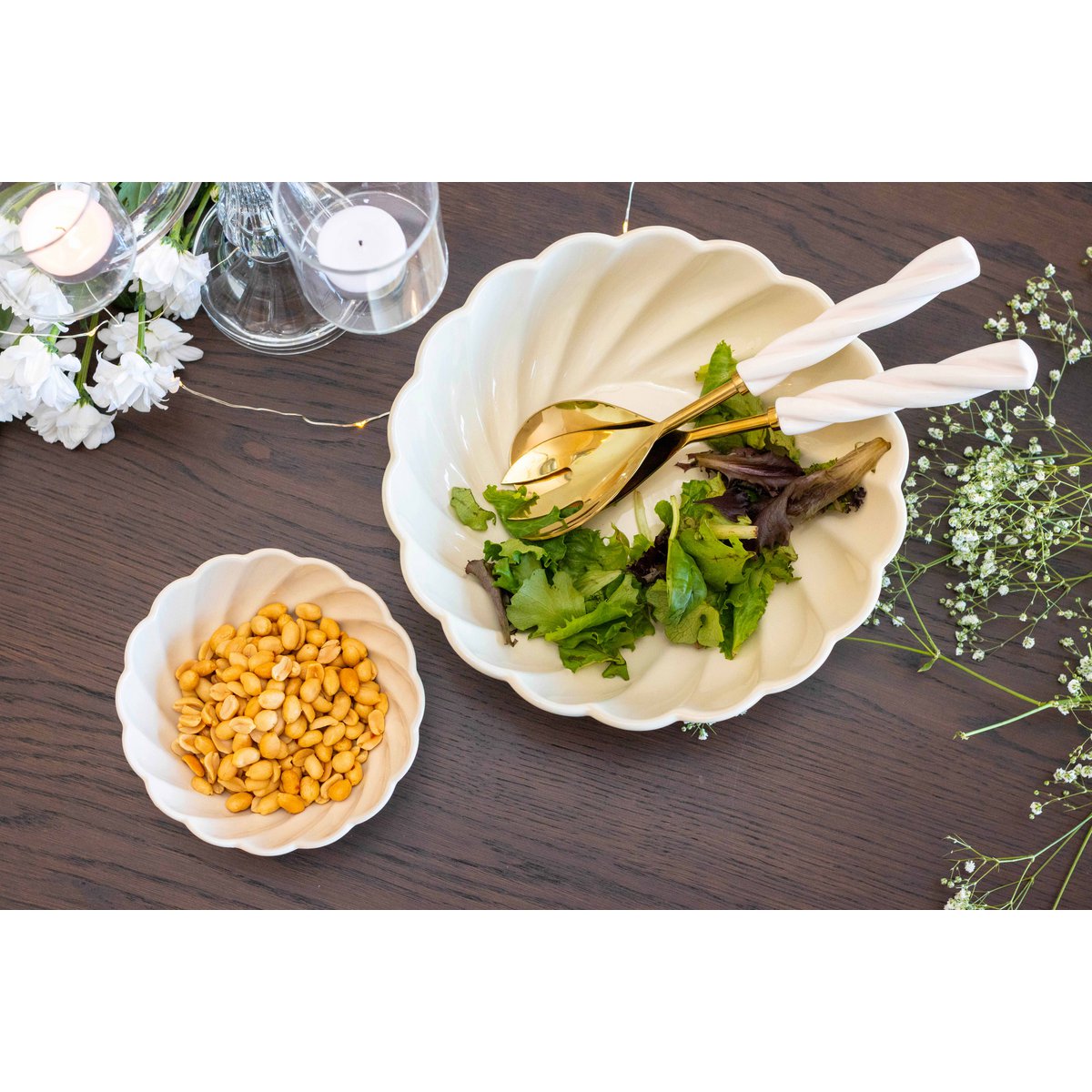 Two white bowls on a wooden table, one with salad and the other with beans, surrounded by flowers.